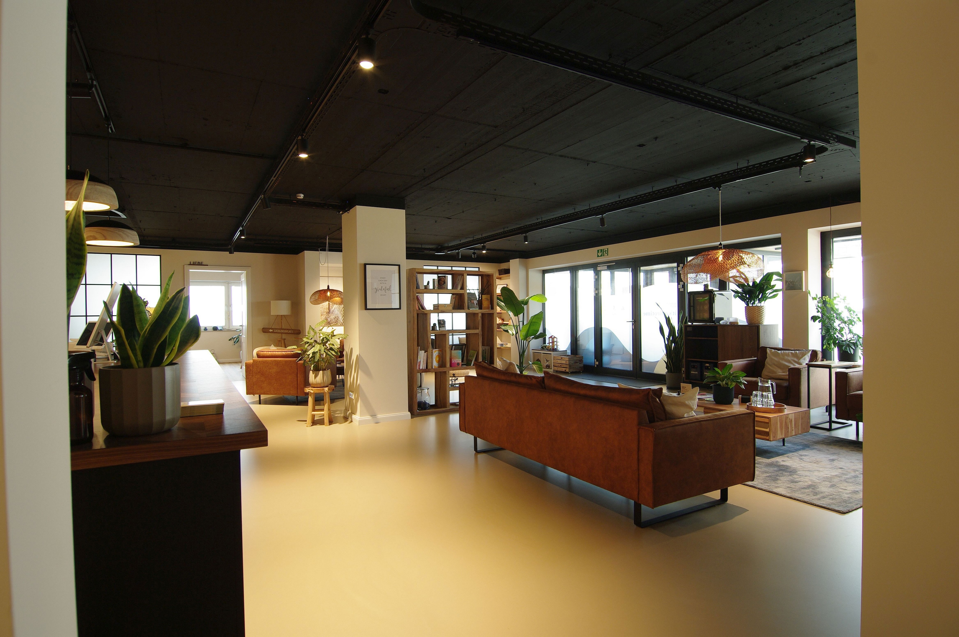 Wartebereich mit Sofas, Holzregal und Pflanzen entlang der Fensterfront der Chiropraxis — Praxisumbau von Bernd Schüller
