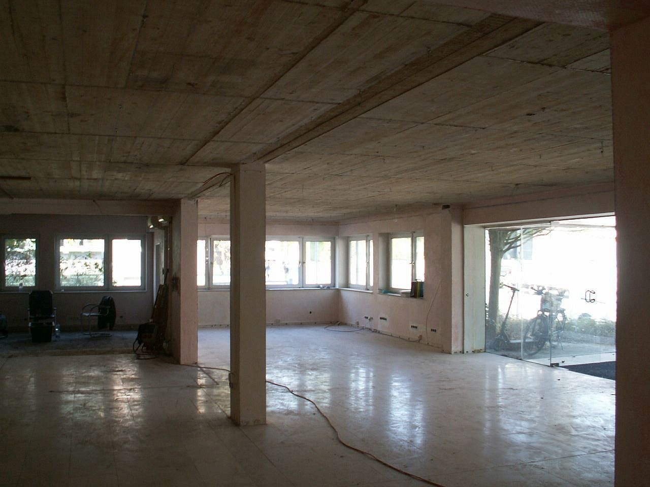 Leere Büroetage mit Betonstützen, Fensterfront und Glaseingang vor dem Umbau zur Chiropraxis