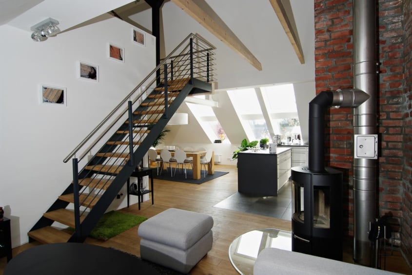 Das Prinzip Dachwohnung. Dachgeschossumbau im Denkmal., Düsseldorf-Oberrath — Blick von der Treppe auf den Wohnbereich mit Kaminofen und Edelstahl-Abluftrohr