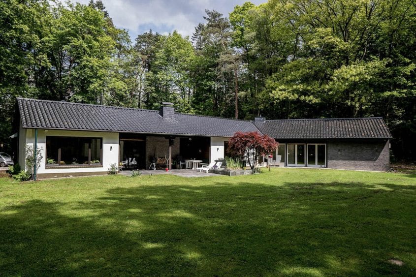 Entwurf im Waldhaus, Mönchengladbach-Hardt — Eingeschossiges Haus mit dunklem Ziegeldach und Terrasse, umgeben von dichtem Baumbestand