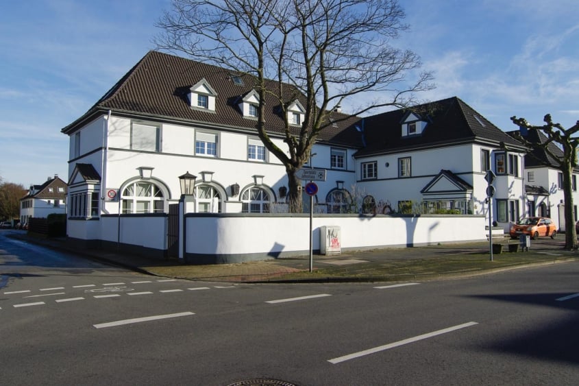 Sanierung historischer Bausubstanz, Monheim am Rhein — Straßenecke des ehemaligen Bade- und Waschhauses von 1916 mit weißer Putzfassade und Dachgauben