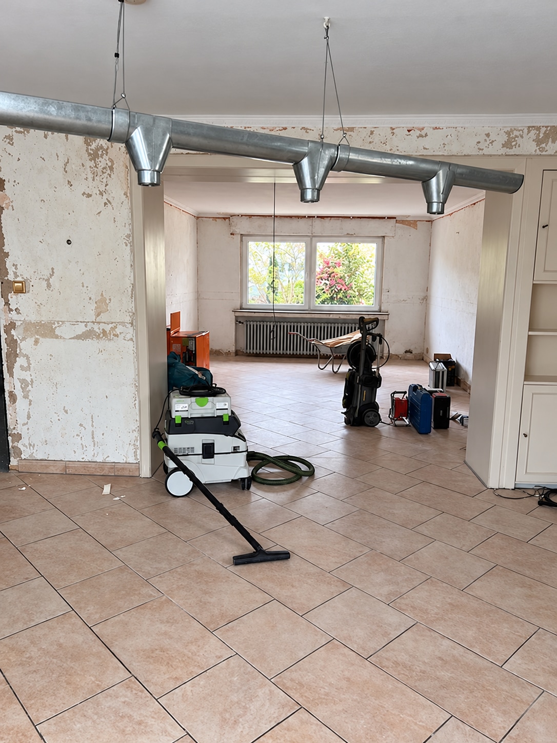 Entkernter Wohnraum mit Fliesenboden, Lüftungsrohr und Baugeräten